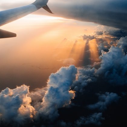 Sun comes out from the clouds below an airplane, through airplane window