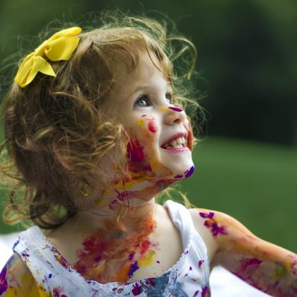 A young girl, covered in paint, smiling widely