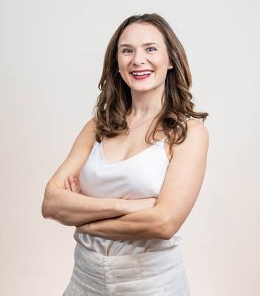 Dr Amelia Lambers smiles at the camera. She is standing up with her arms crossed, wearing an all white outfit
