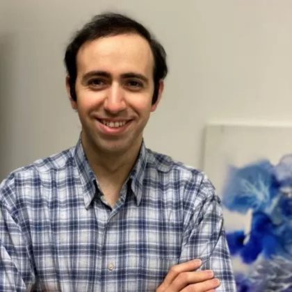 Dr Arash V. Esfahani smiles at the camera. He is wearing a white and blue flannel shirt and has short dark hair.